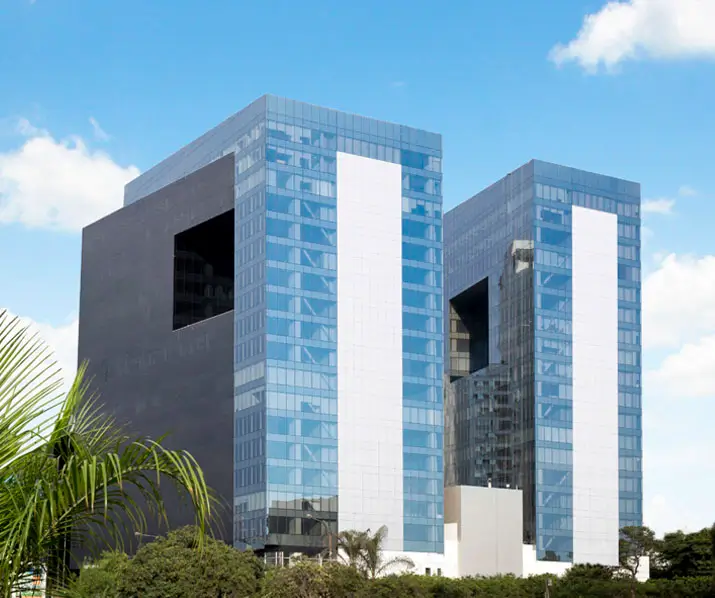 Dos imponentes edificios de vidrio y hormigón, con grandes ventanales y un diseño moderno, rodeados de vegetación.