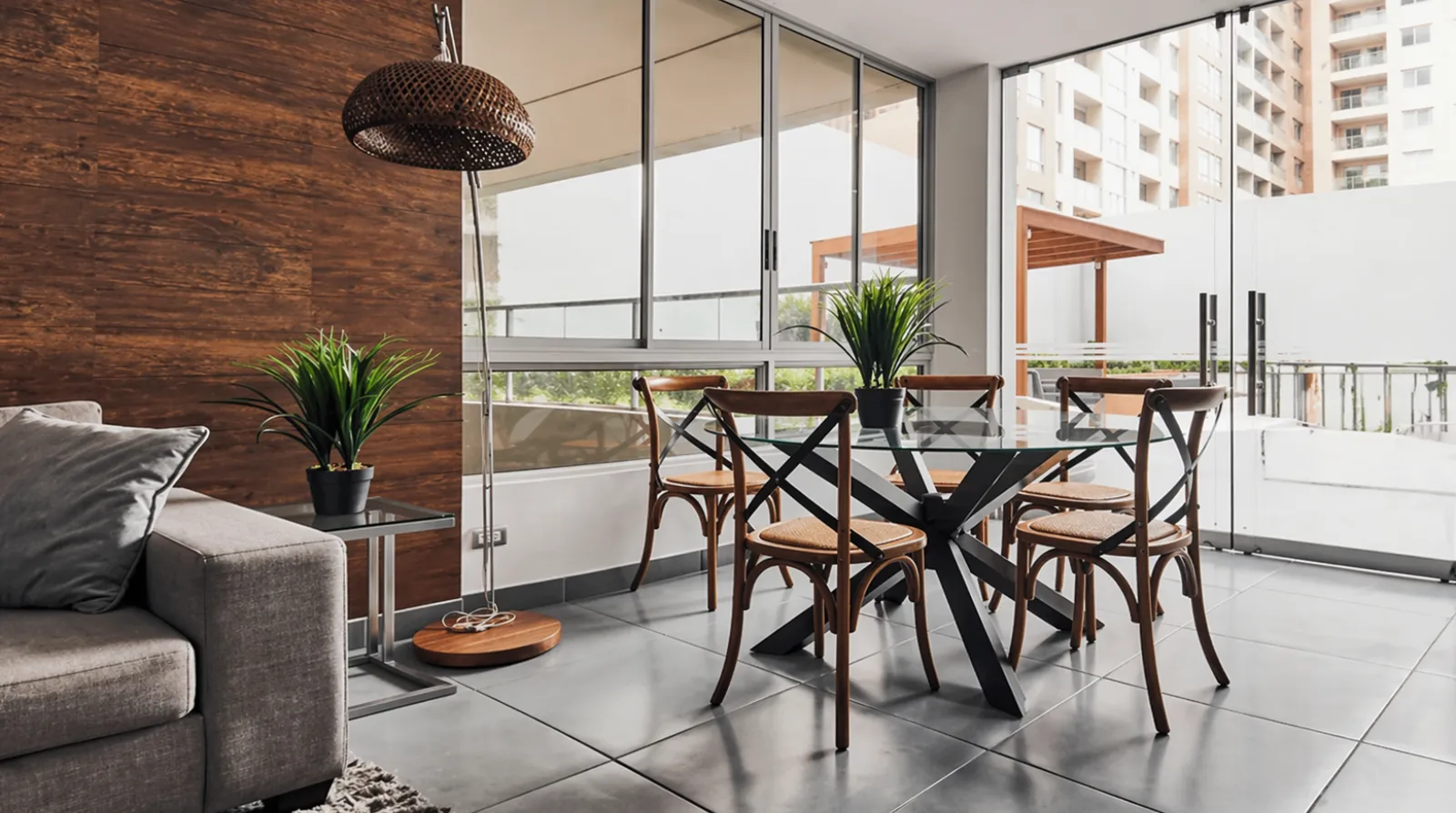 Comedor moderno con mesa de cristal y sillas de madera junto a ventanales grandes. Decoración minimalista con plantas.