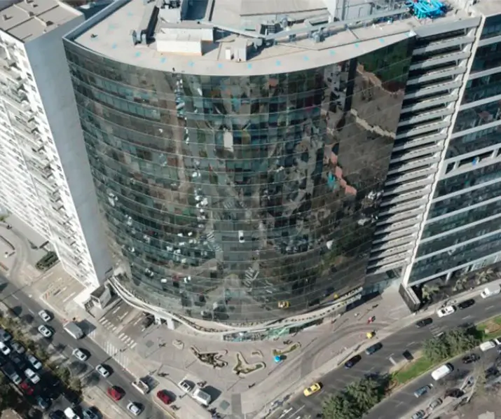 Edificio moderno con fachada de vidrio reflejante en zona urbana, rodeado de tráfico y áreas verdes.