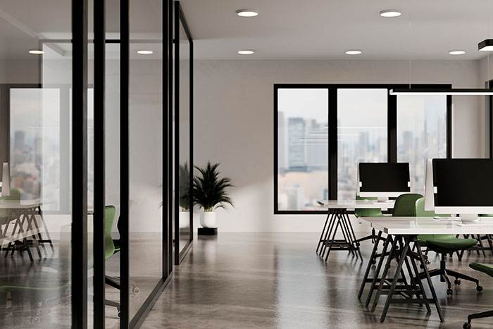 Oficina moderna con escritorios verdes, paredes de vidrio y ventanas panorámicas que ofrecen vistas urbanas.