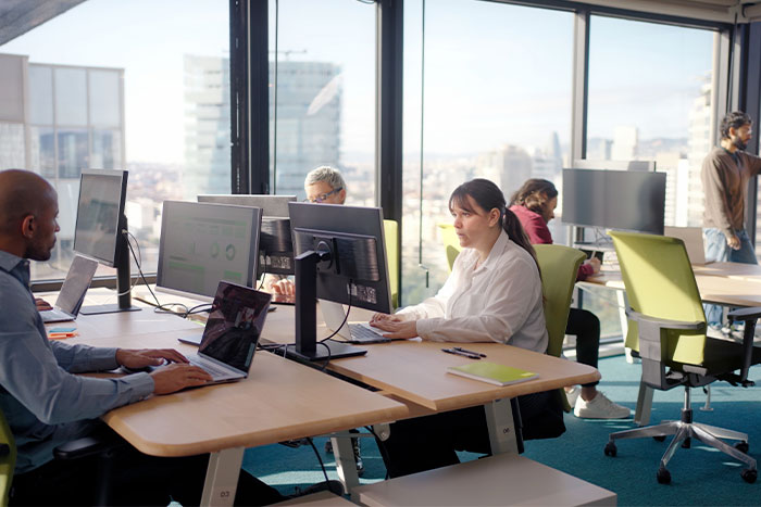 Empleados trabajando en un moderno espacio de oficina, con computadoras y vistas panorámicas de la ciudad.