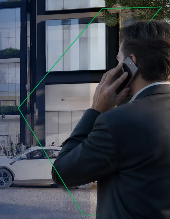 Hombre de negocios hablando por teléfono frente a una moderna edificación, con autos y viandantes al fondo.
